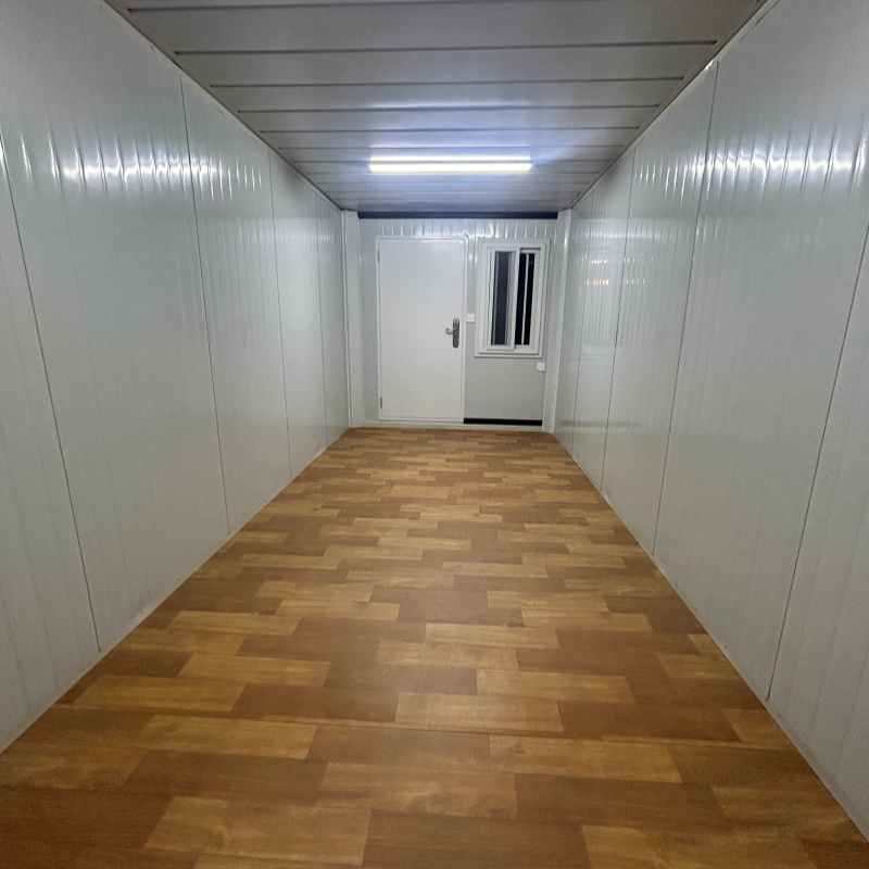 Interior view of a modern folding container house featuring a spacious open-plan layout, wooden laminate flooring, LED ceiling lights, and white sandwich panel walls.