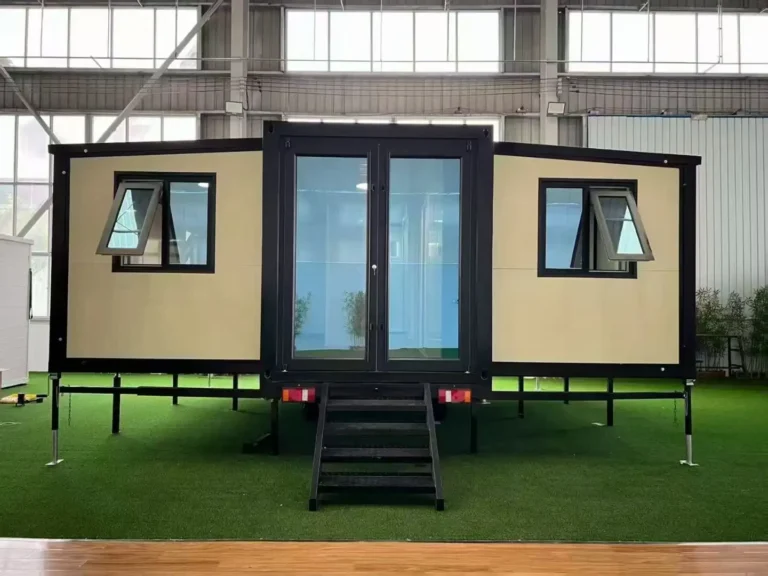 A sleek cream-and-black South Africa expandable container house project unit featuring a central glass double-door entry, black-framed awning windows, and an elevated steel foundation with black entry stairs.