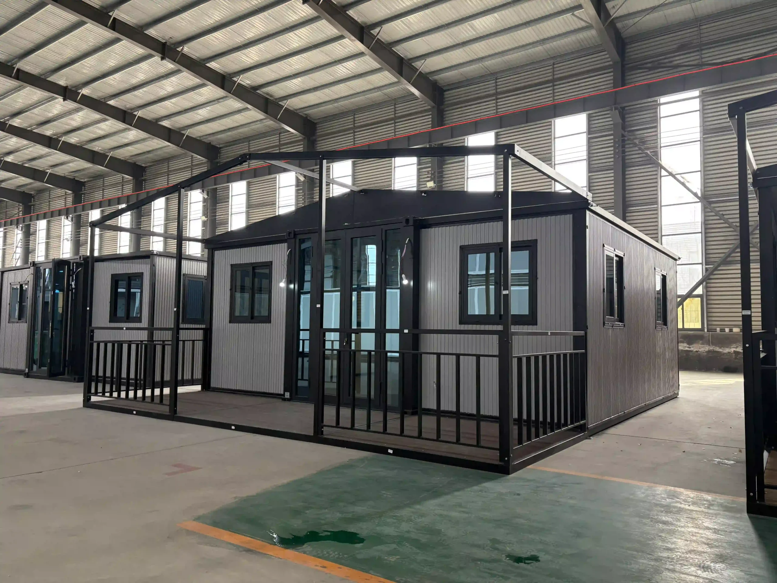 Une annexe extensible entièrement déployée à l'intérieur d'un site de production, présentant une élégante extérieur en tôle ondulée gris clair, des portes d'entrée vitrées à cadre noir et une véranda intégrée avec garde-corps de sécurité.