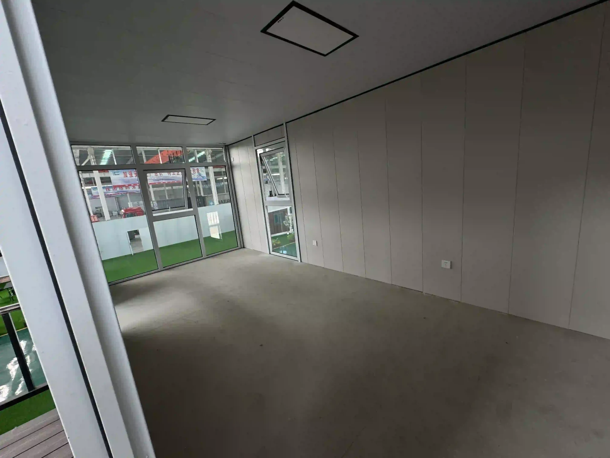 A stunning two-story stacked shipping container house featuring an offset upper level that creates a natural balcony, finished in a minimalist grey industrial coating with floor-to-ceiling glass panoramic windows.