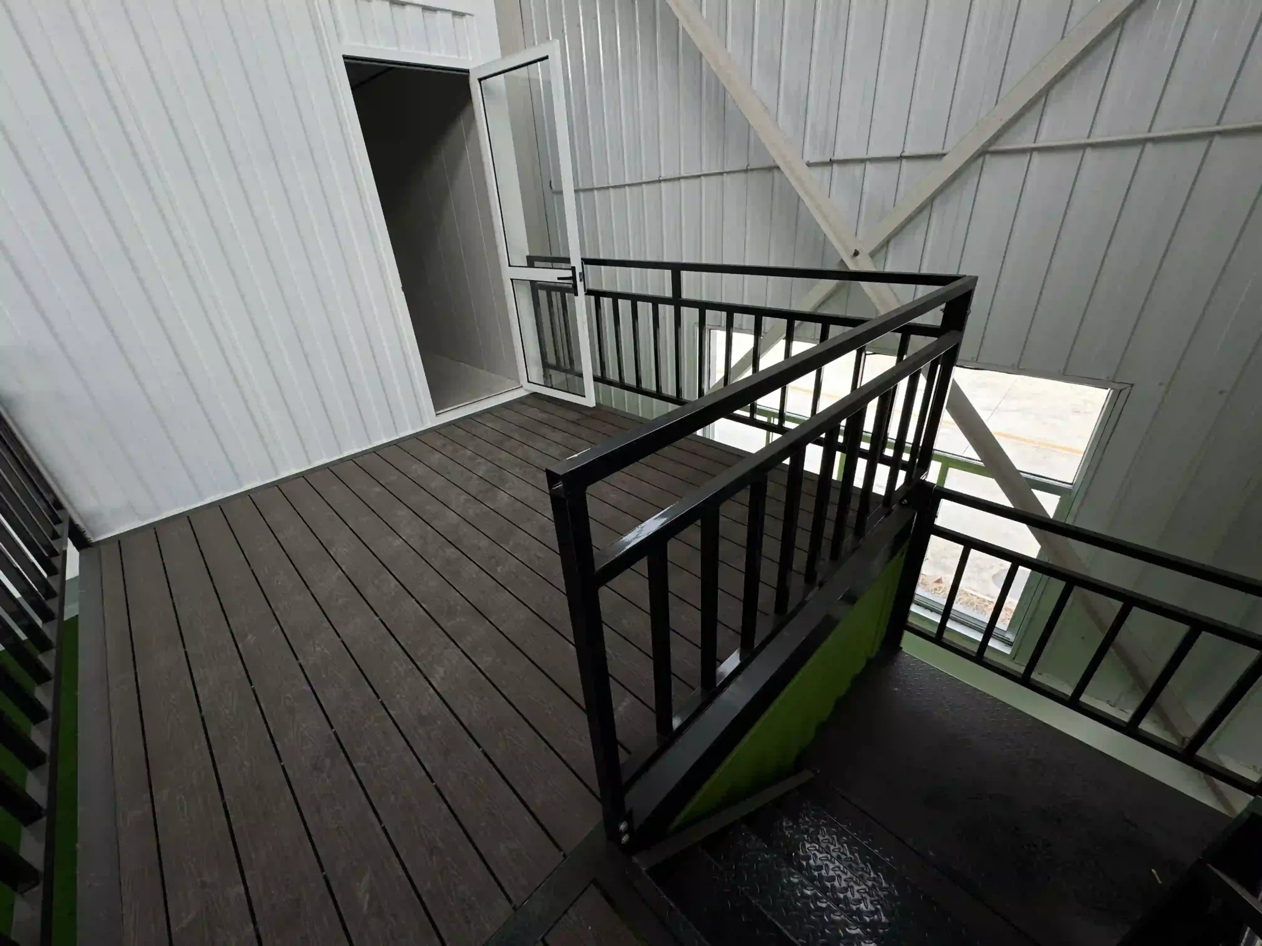 A modern two-story stacked shipping container house featuring an offset upper level with a spacious balcony, floor-to-ceiling glass windows, and a sleek industrial grey finish.